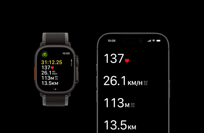 블랙 색상 티타늄 케이스의 Apple Watch Ultra 3와 블랙/차콜 색상 트레일 루프, iPhone, 그리고 두 기기에 활성화된 운동 수치가 표시된 모습
