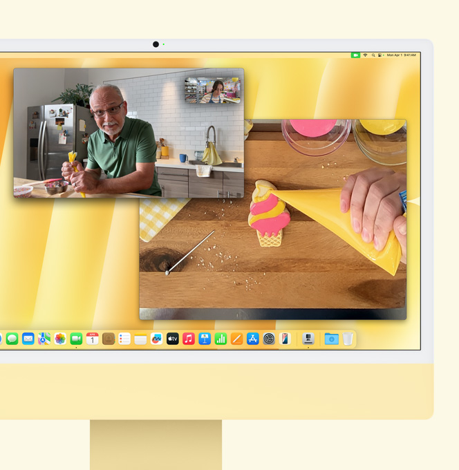 黃色 iMac。桌上視角功能示範。螢幕顯示烘焙師在與別人進行視像通話。一個畫面顯示烘焙師和一位男士的臉，另一個畫面顯示烘培師的手在曲奇上擠糖霜
