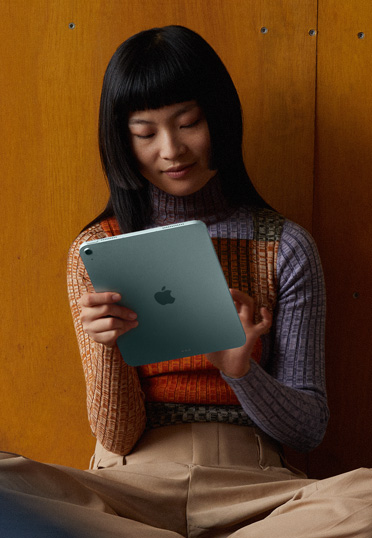 Una estudiante sentada en el piso y recostada a la pared sostiene un iPad.