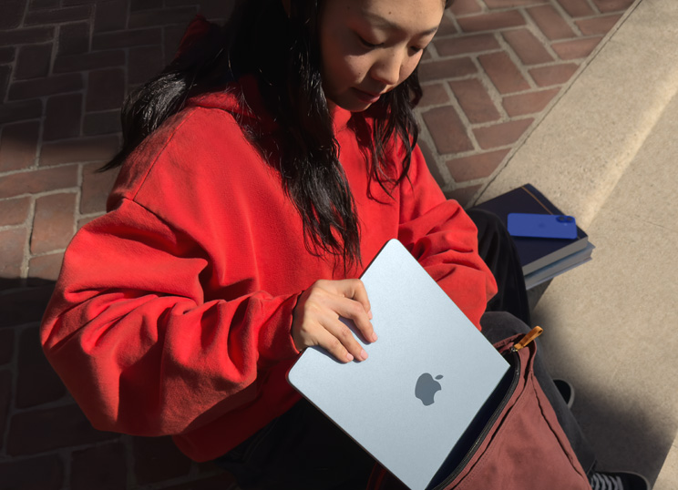 Person sitting on stone steps placing MacBook into backpack.