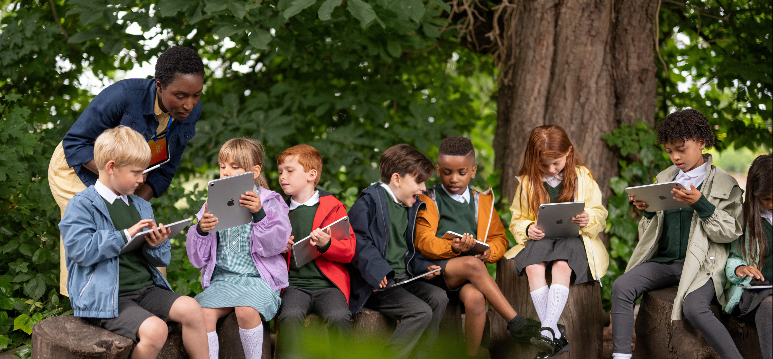 一群年幼學生在户外使用 iPad，導師拿著 iPad 引導他們，突顯學習不受時間和地點限制