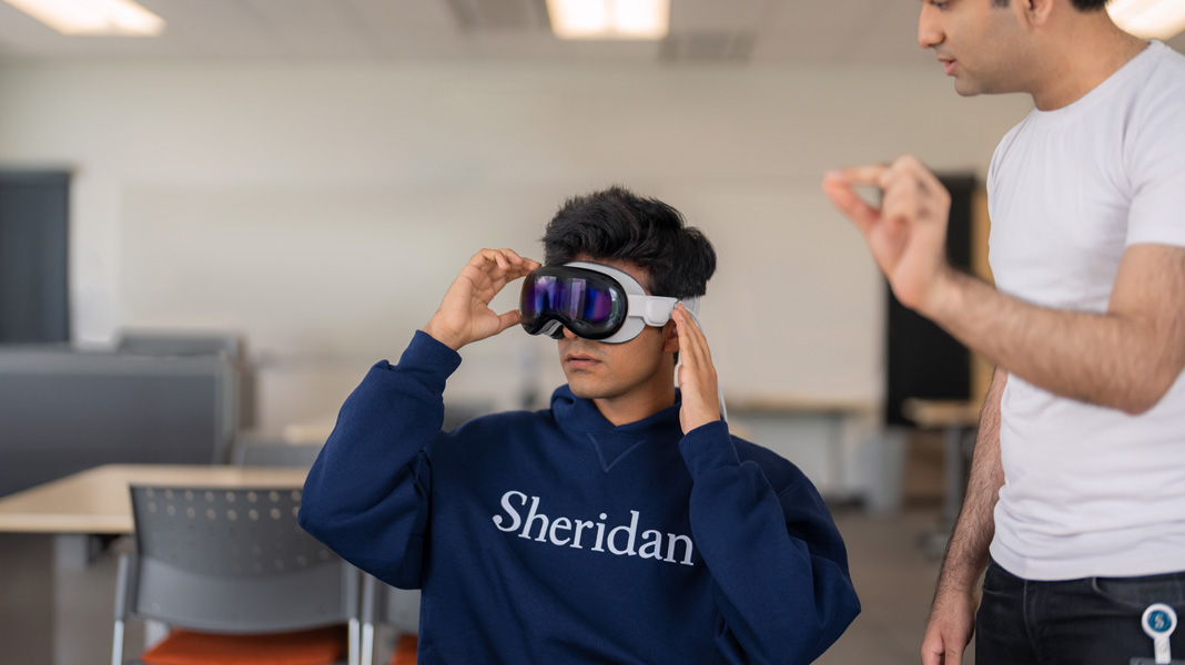 A student wearing a Sheridan sweatshirt tries on a mixed-reality headset.
