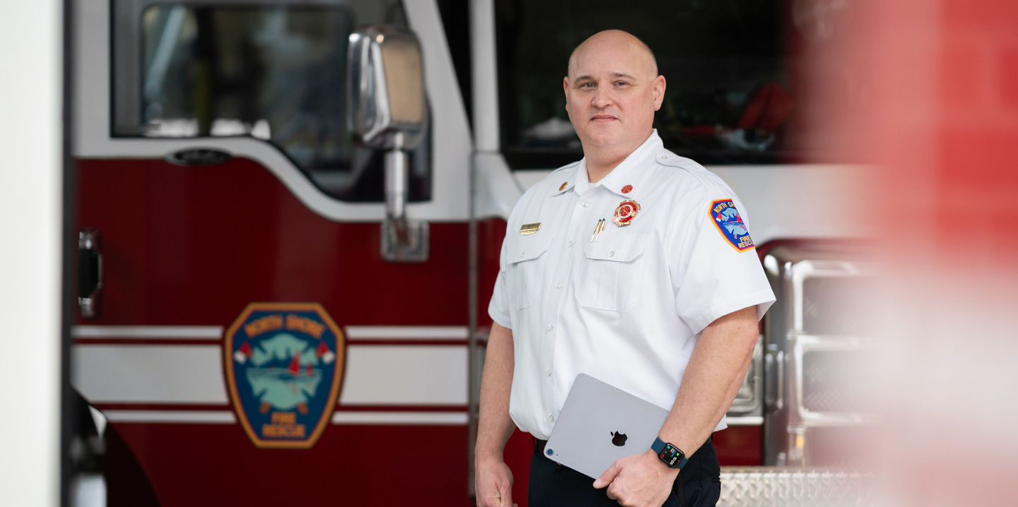 Chefe dos bombeiros em frente a um caminhão, segurando um iPad e usando um Apple Watch