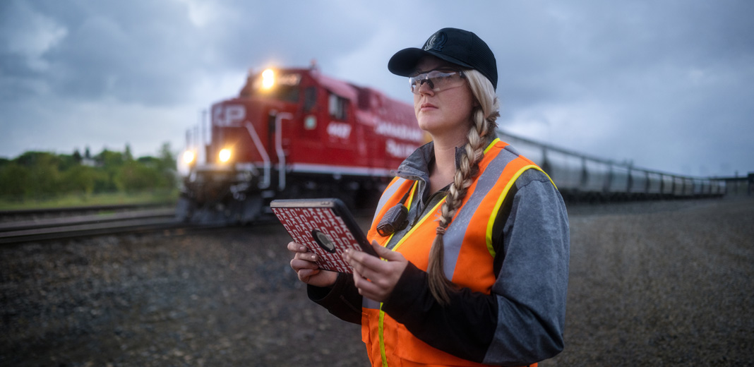 Uma funcionária da ferrovia segura um iPad e observa os trilhos enquanto um trem passa