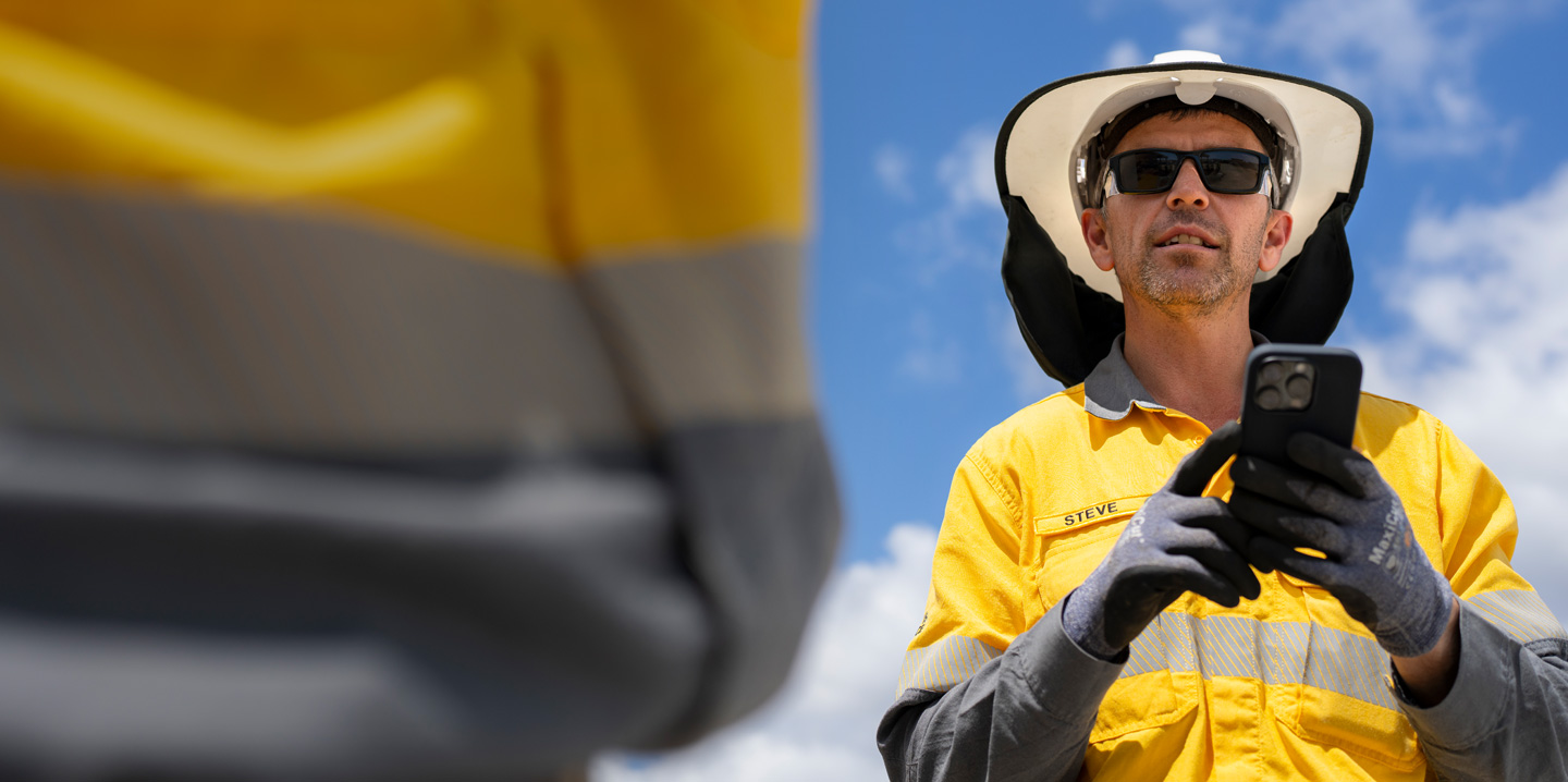 Uma pessoa da equipe de campo vestindo equipamento de proteção segura um iPhone enquanto conversa com alguém