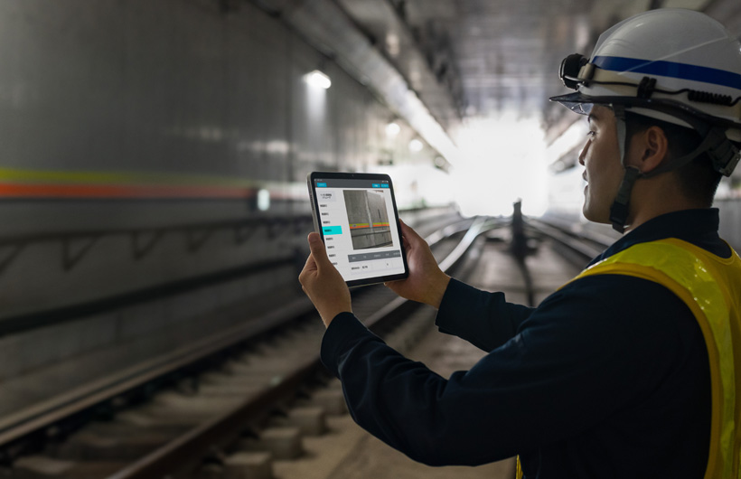 Ein Wartungsarbeiter in den Tunneln der Tokyo Metro hält ein iPad hoch, um ein Bild der Gleise aufzunehmen, während sein Kollege zusieht.