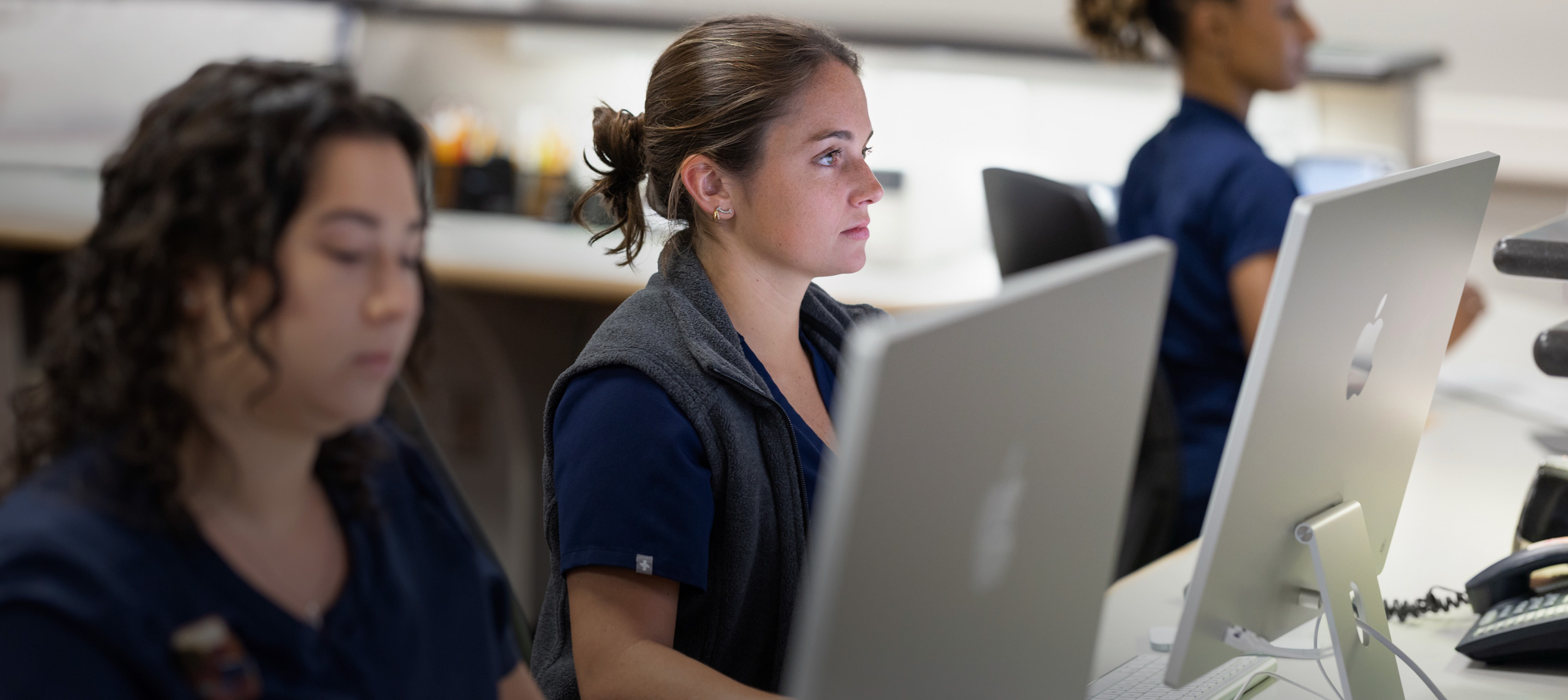 Drie verpleegkundigen aan het werk achter iMac-schermen.