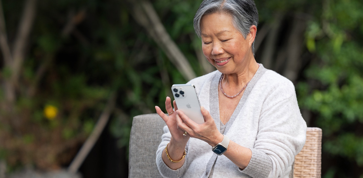 Een oudere vrouw zit in een stoel en kijkt naar een iPhone.