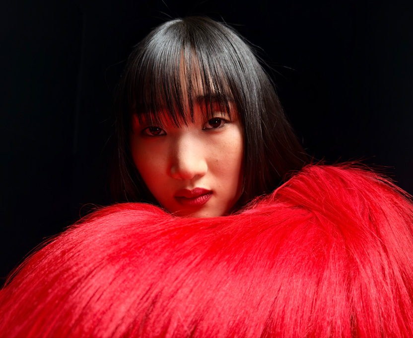 Photo en gros plan d’une femme vêtue d’un haut à plumes rouge vif illustrant les capacités photographiques extra haute définition d’iPhone 17 Pro