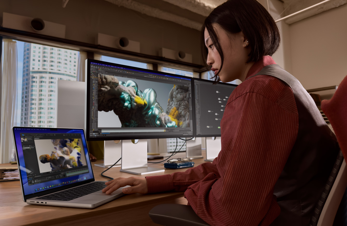 Una persona en una oficina trabaja en un portátil MacBook conectado a un monitor Studio Display XDR mediante un puerto Thunderbolt 5